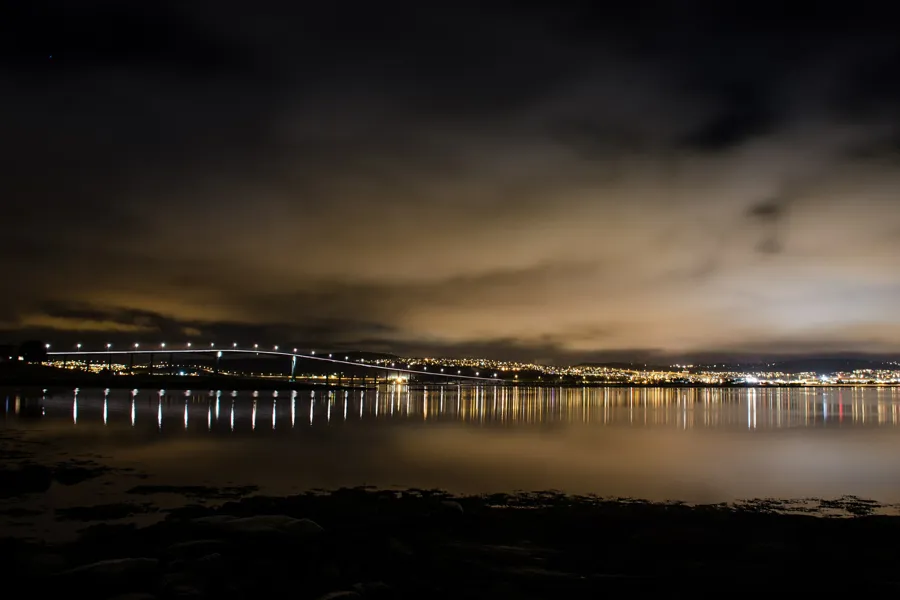 Tromsøbrua på kveldstid. Lys fra brua og bebyggelse.