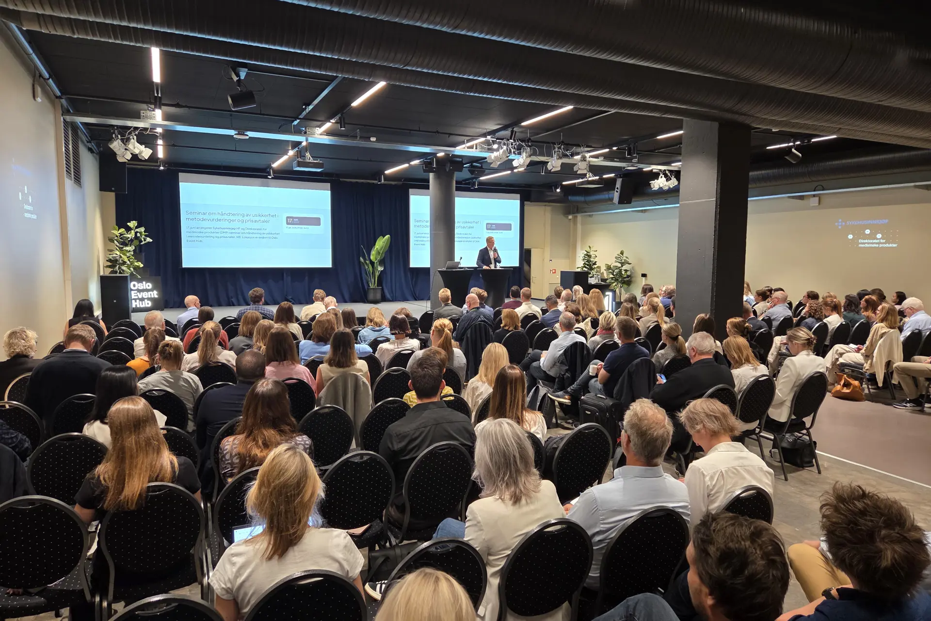 En gruppe mennesker som sitter i et rom med en stor skjerm