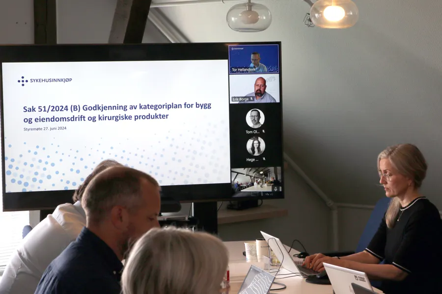 Flere personer sitter rundt et møtebord. En skjerm viser et saksdokument.