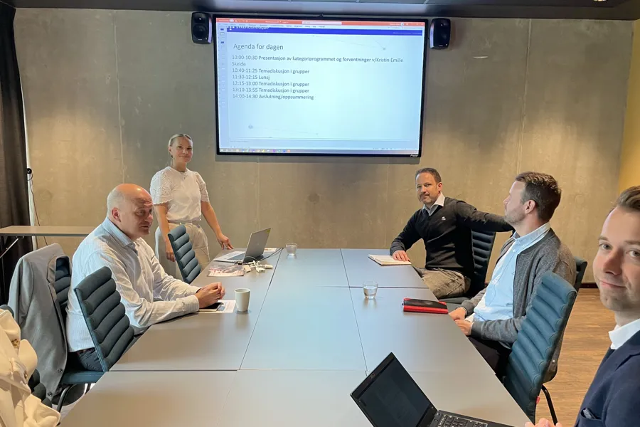 En gruppe menn som sitter rundt et bord med en projektorskjerm