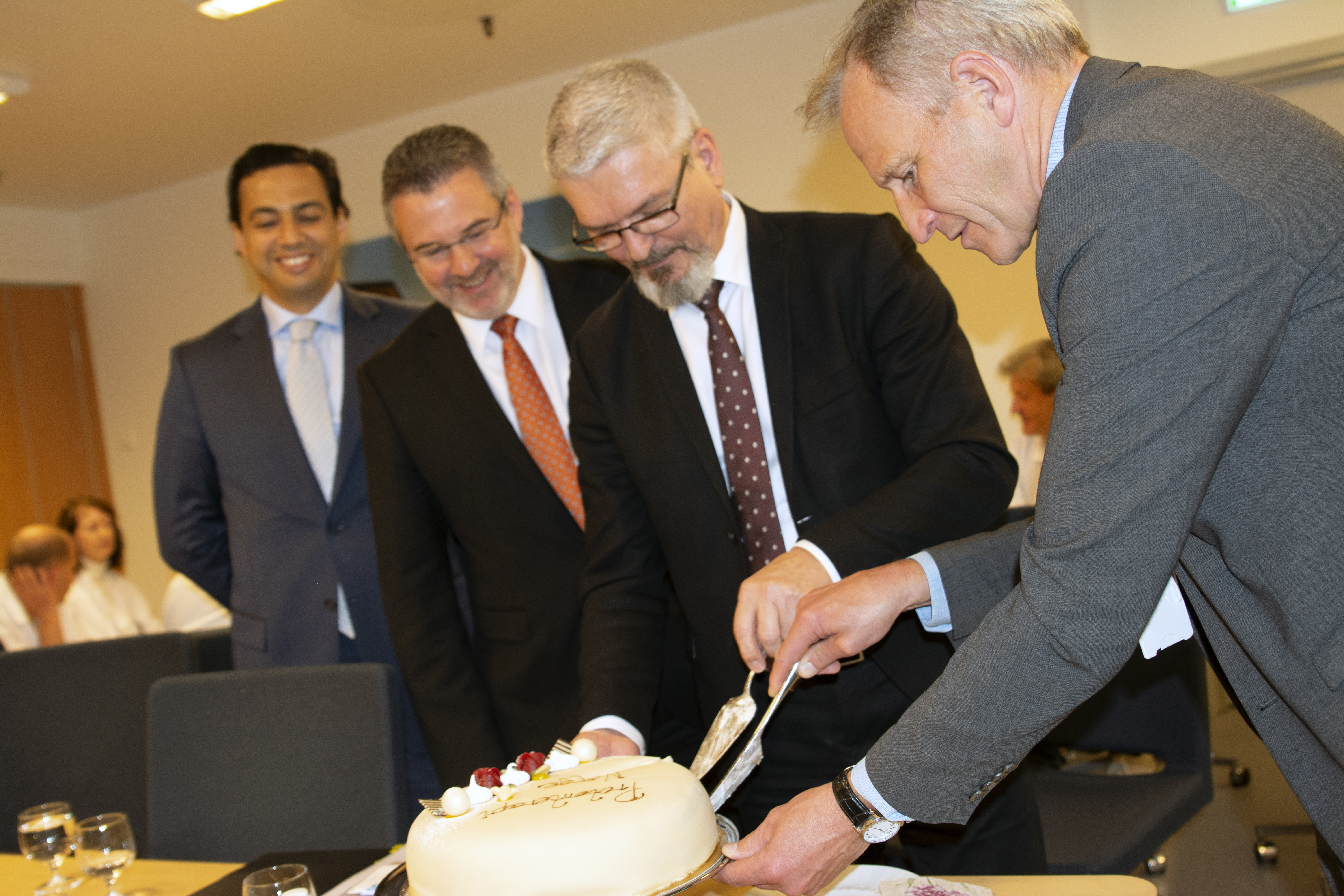 Fire menn står ved en kake som skjæres opp under feiring av kontraktsigneringen.